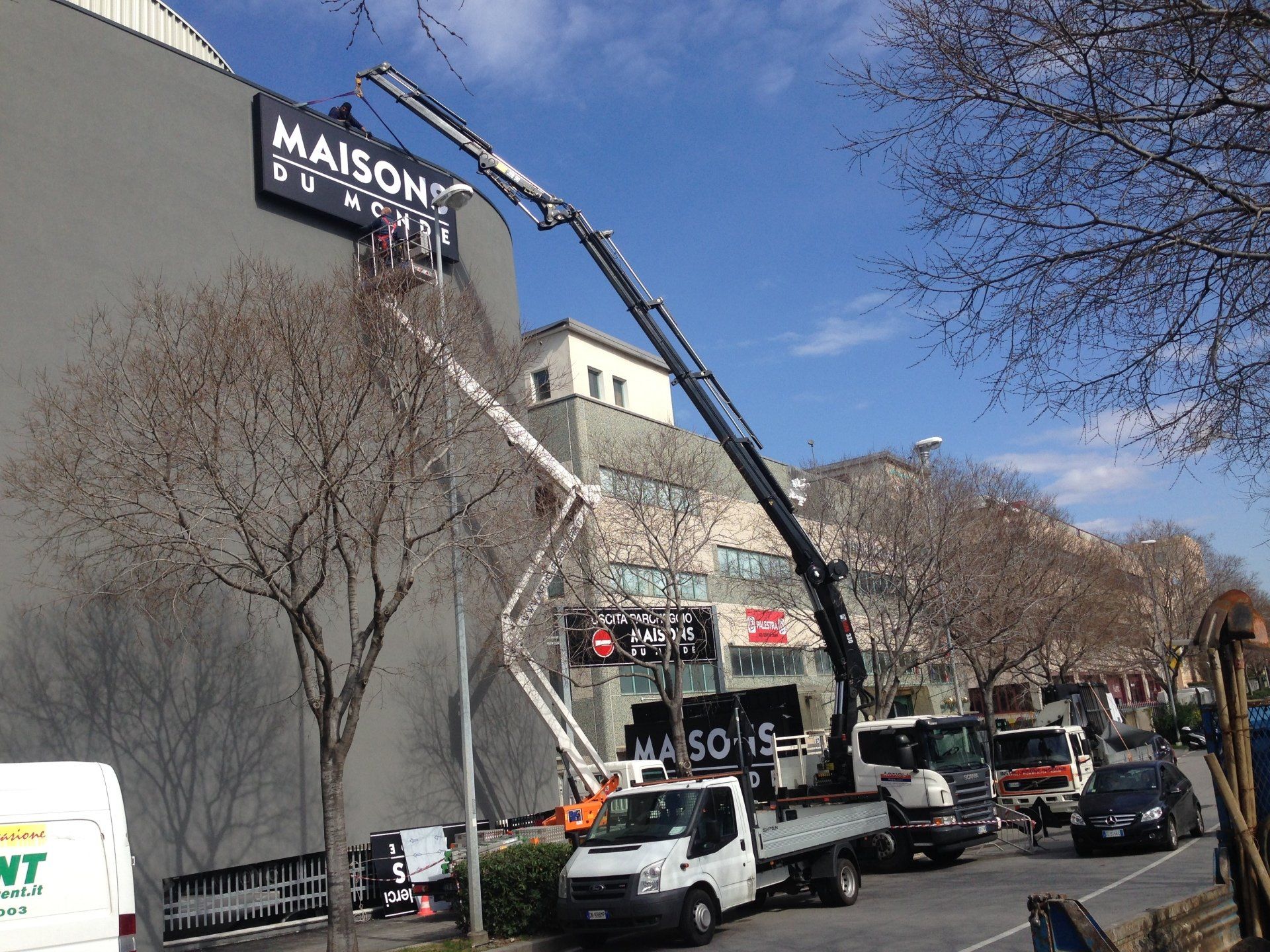 Operai su un ascensore che installano un cartello sulla facciata di un edificio, scena di strada.