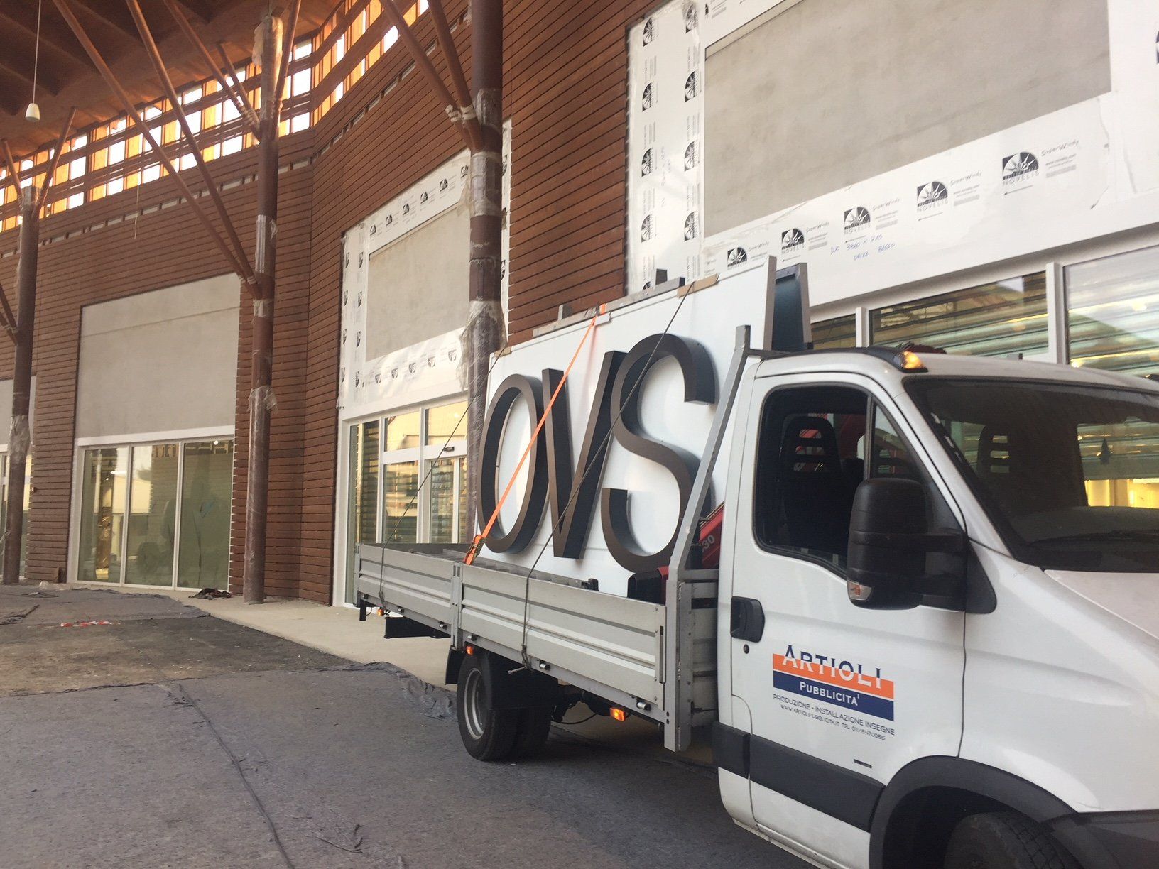 Camion bianco con la scritta OVS parcheggiato vicino a un edificio in mattoni.