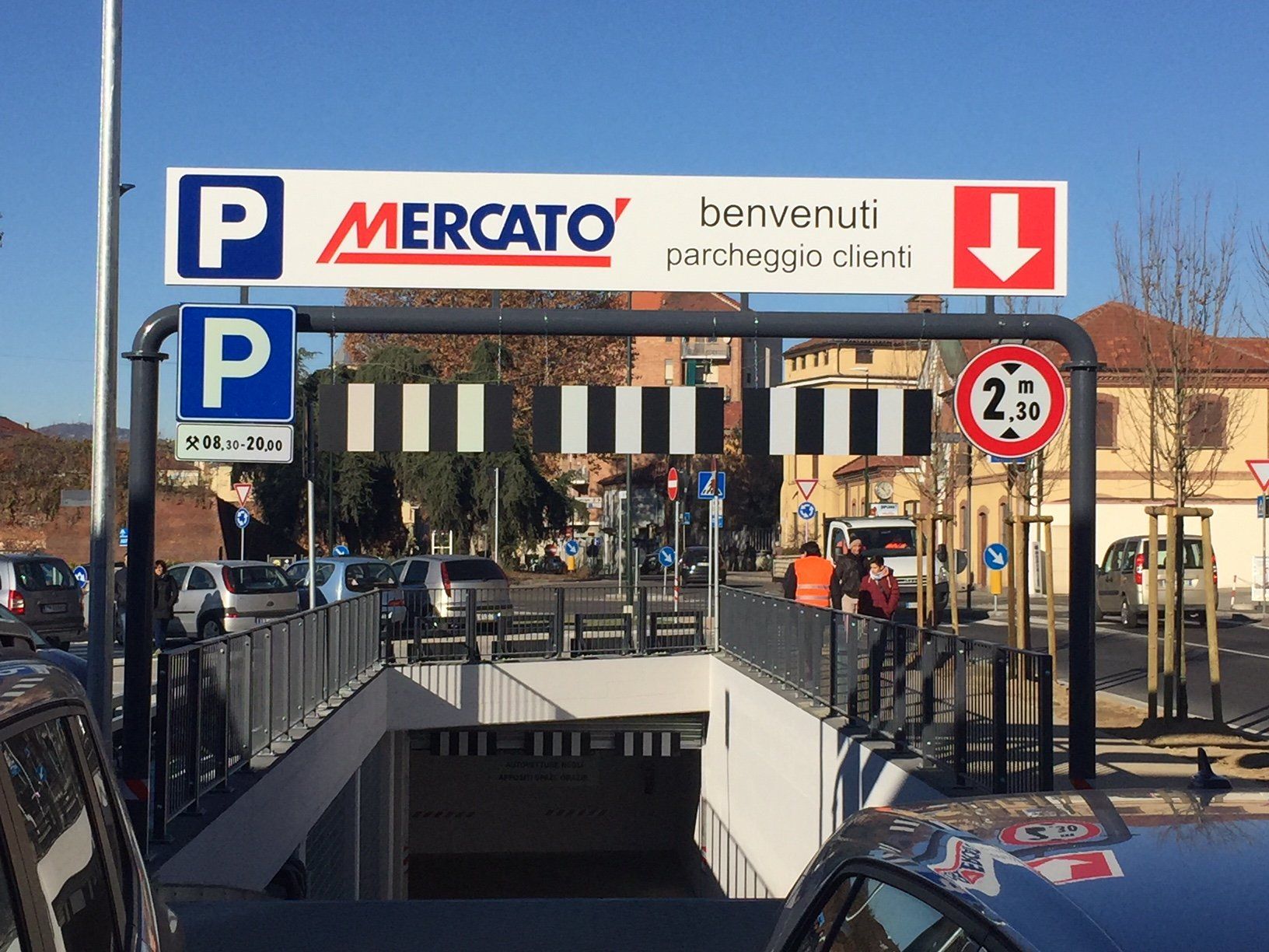 Ingresso al parcheggio Mercato con cartelli blu e bianchi, freccia rossa e cartello che indica il limite di altezza.