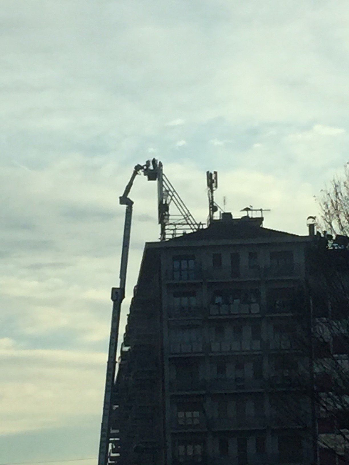 Un alto edificio con una gru che si estende sulla cima contro un cielo nuvoloso.