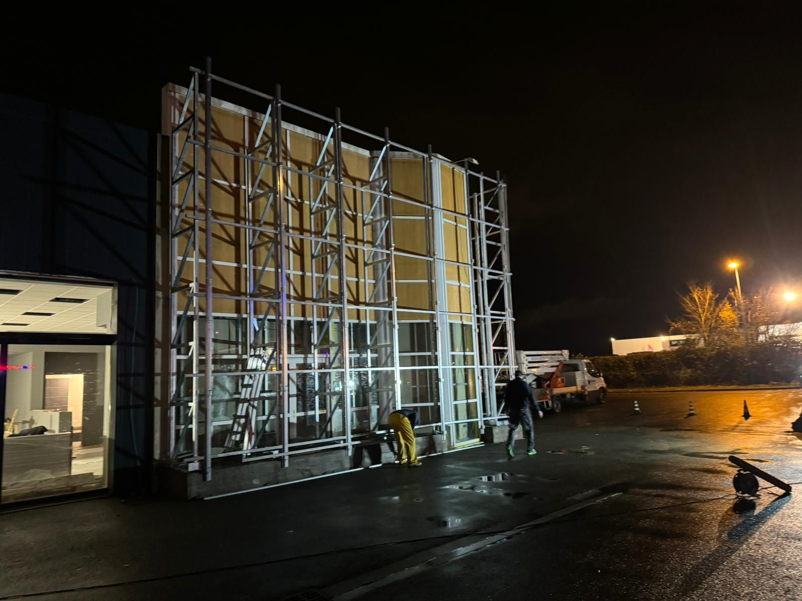 Operai edili vicino alle impalcature di notte; facciata dell'edificio, parcheggio.