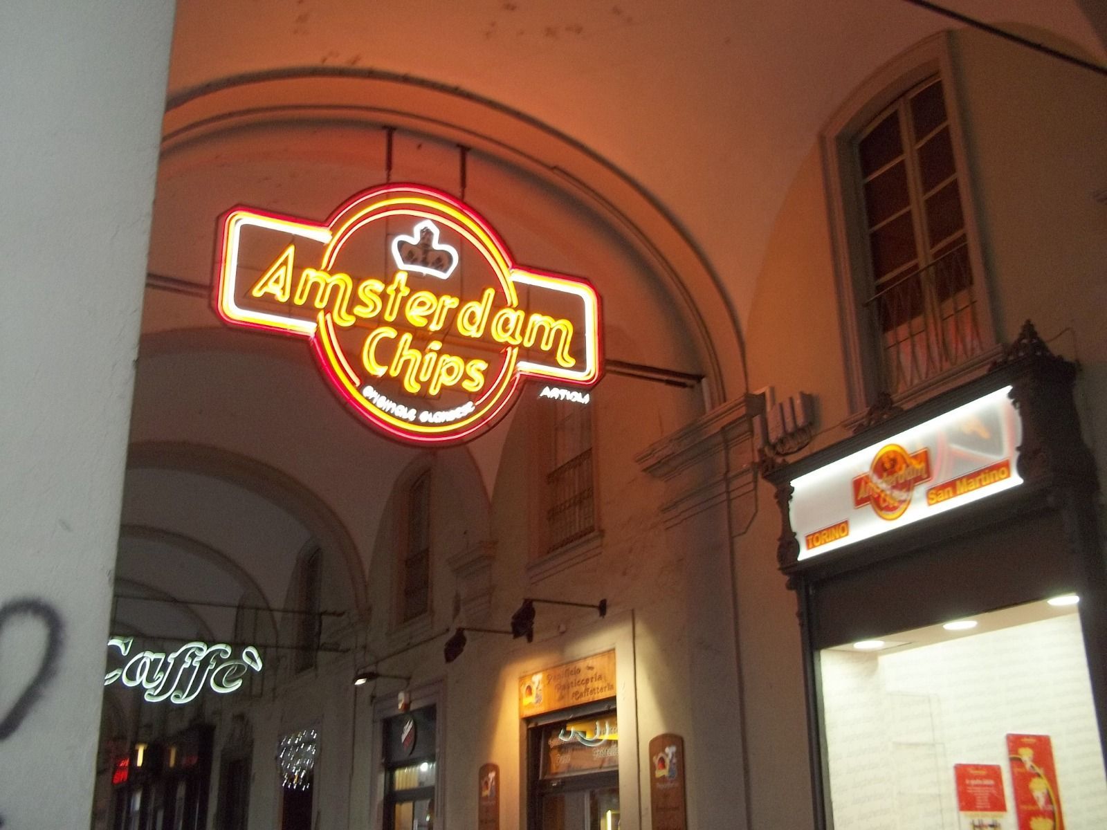 Insegna al neon di Amsterdam Chips in un vicolo ad arco.