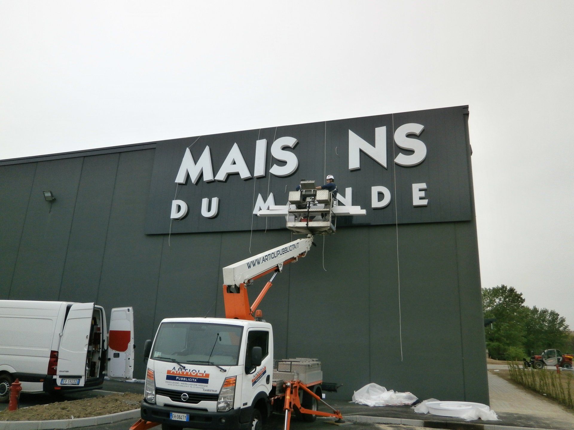 Un operaio su un carrello elevatore installa grandi lettere bianche su un edificio con la scritta 