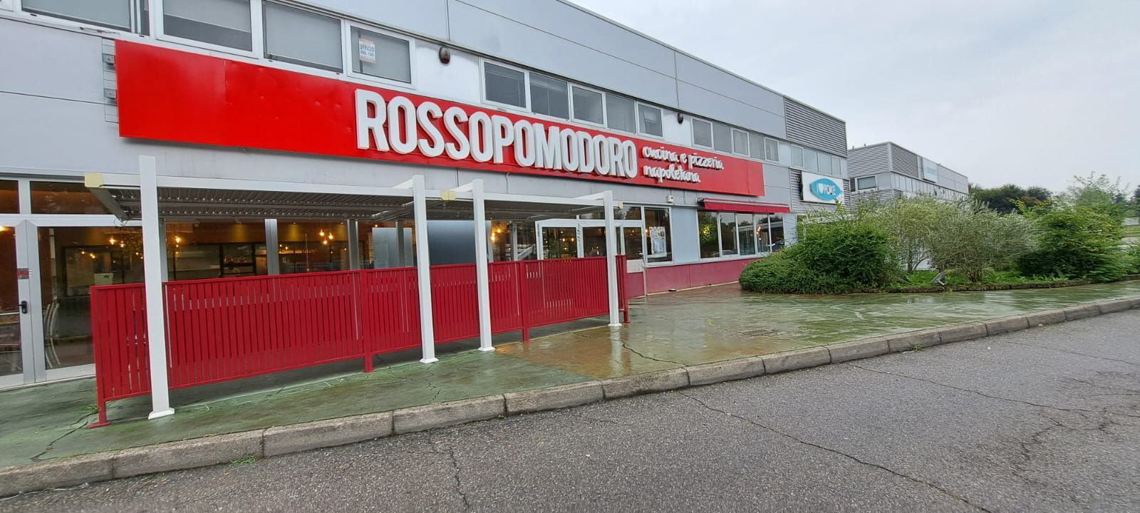 Un ristorante chiamato Rossopomodoro, con un'insegna rossa e una recinzione, che si affaccia su un terreno allagato.