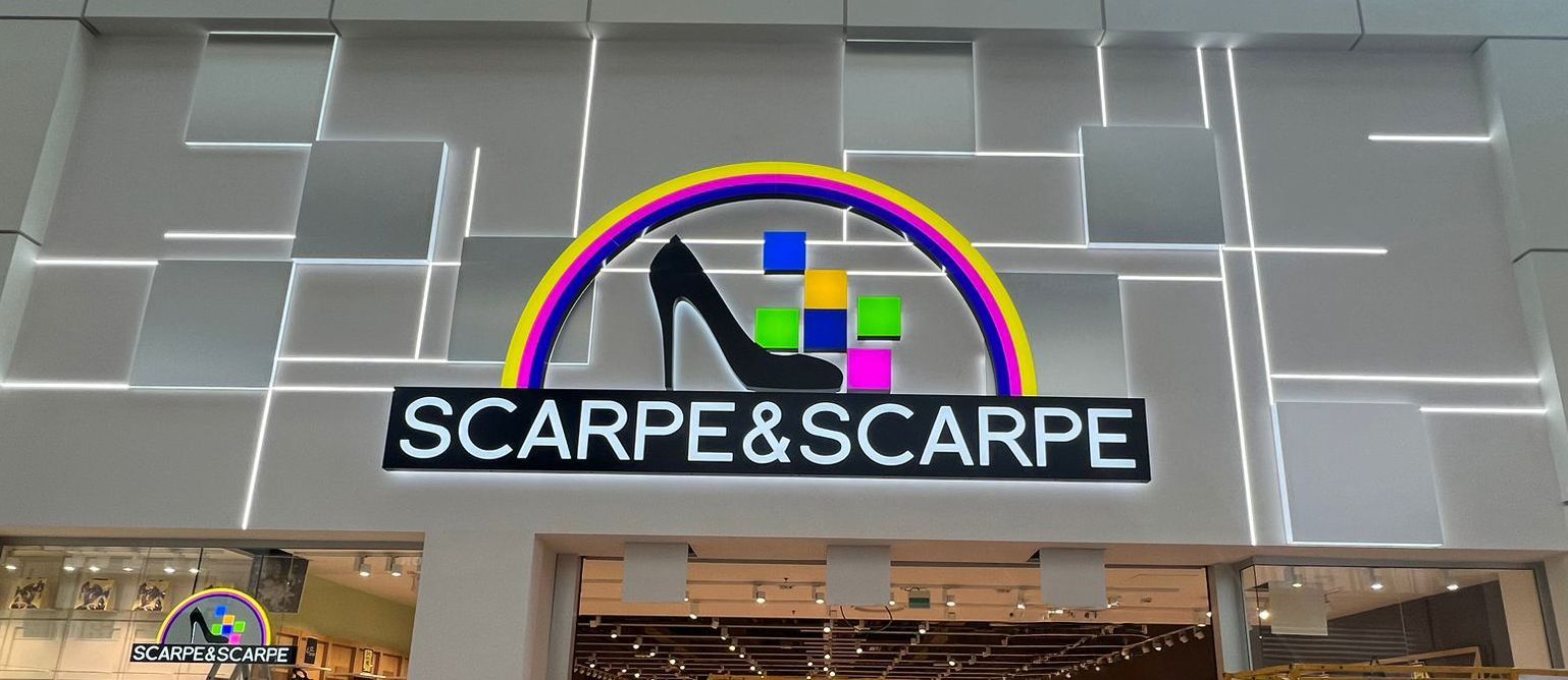 Insegna del negozio di scarpe Scarp&Scarpe con un arcobaleno, un tacco alto e quadrati colorati.