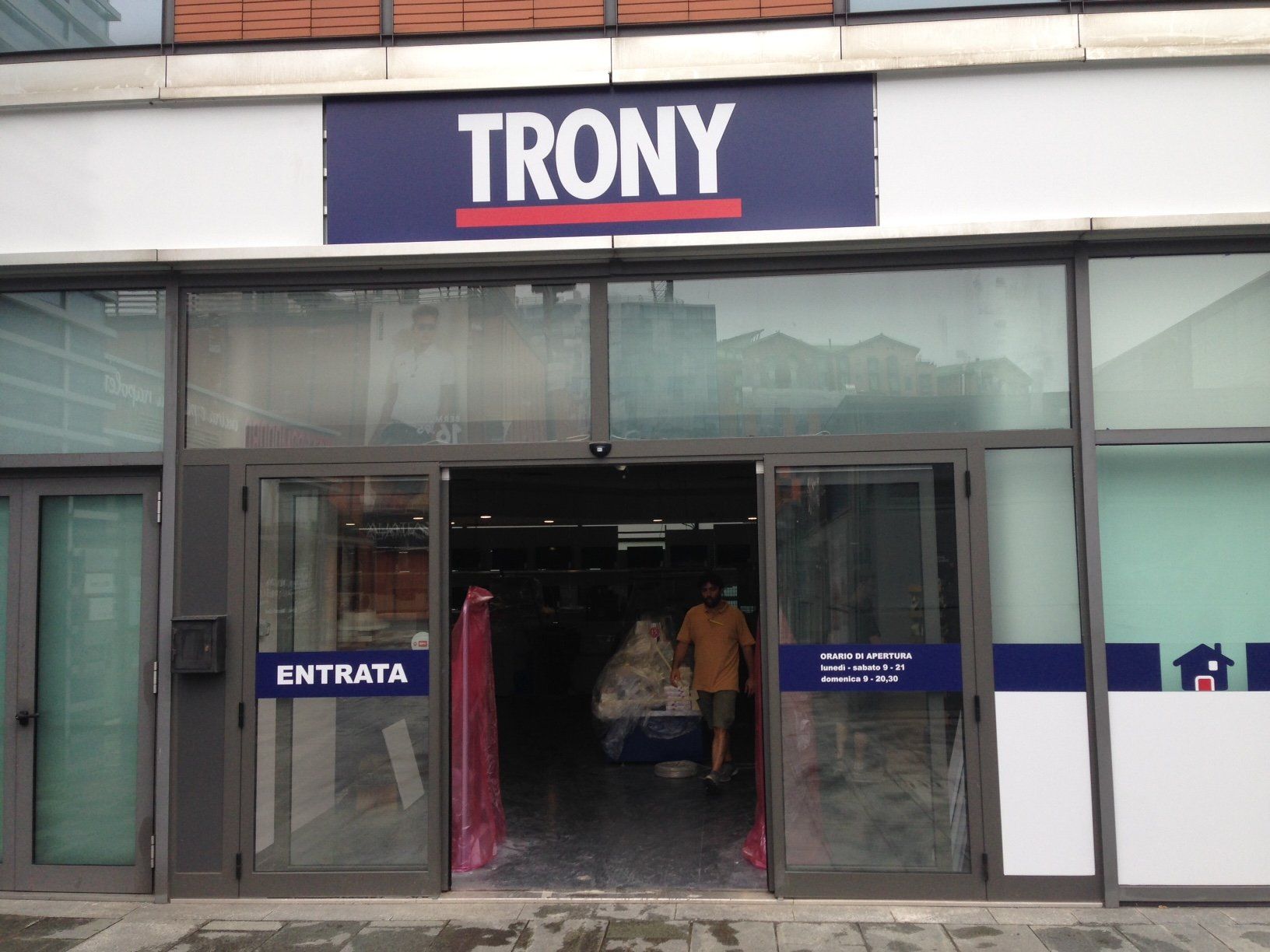 Esterno di un negozio Trony con porte in vetro; insegna blu e rossa sopra l'ingresso; cartello 