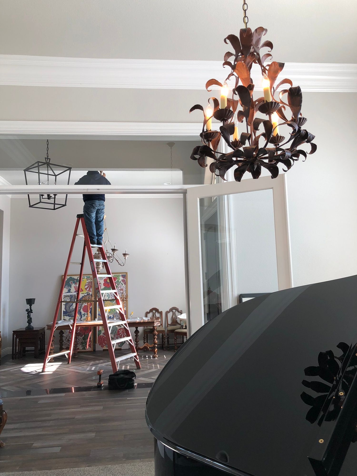 a man on a ladder in a room with a chandelier hanging from the ceiling