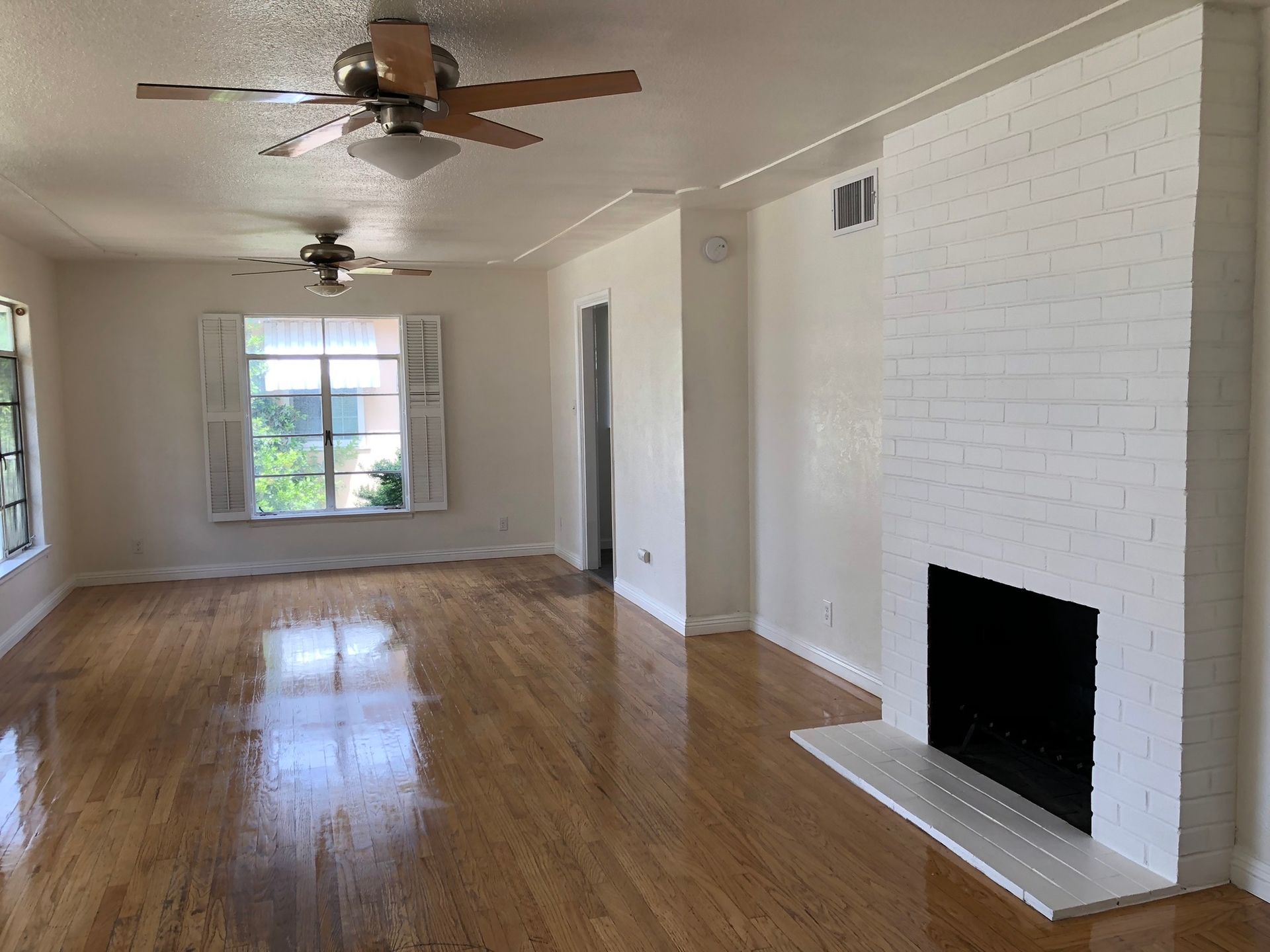 an empty living room with a fireplace and a ceiling fan .