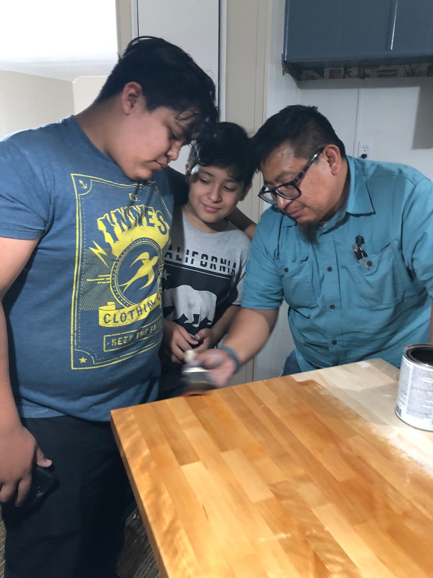 three men are standing around a wooden table looking at a cell phone .