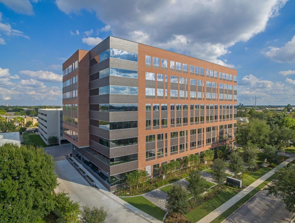 An aerial view of a large brick building with lots of windows surrounded by trees.