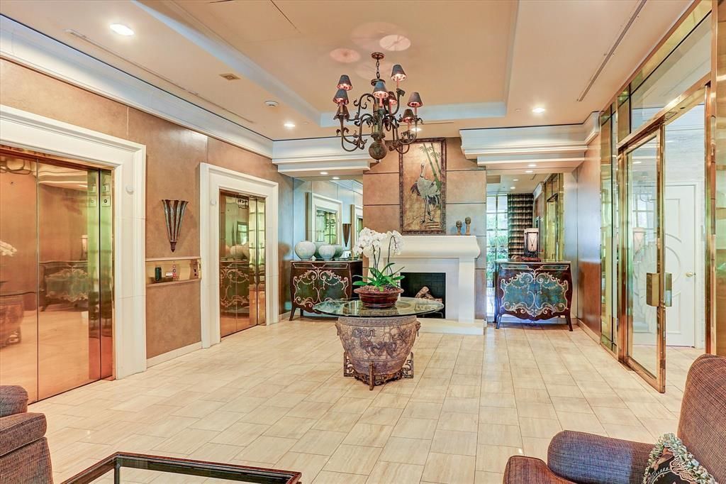 A large lobby with a fireplace , chairs , a table and a chandelier.