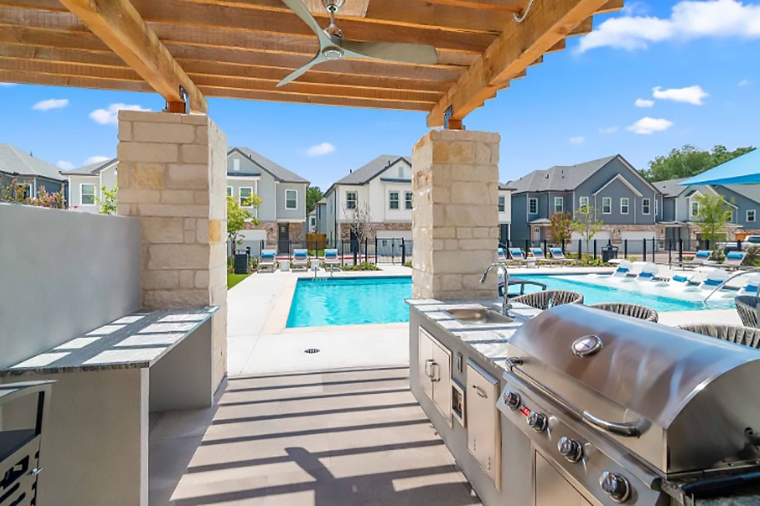 A grill is sitting under a pergola next to a pool.