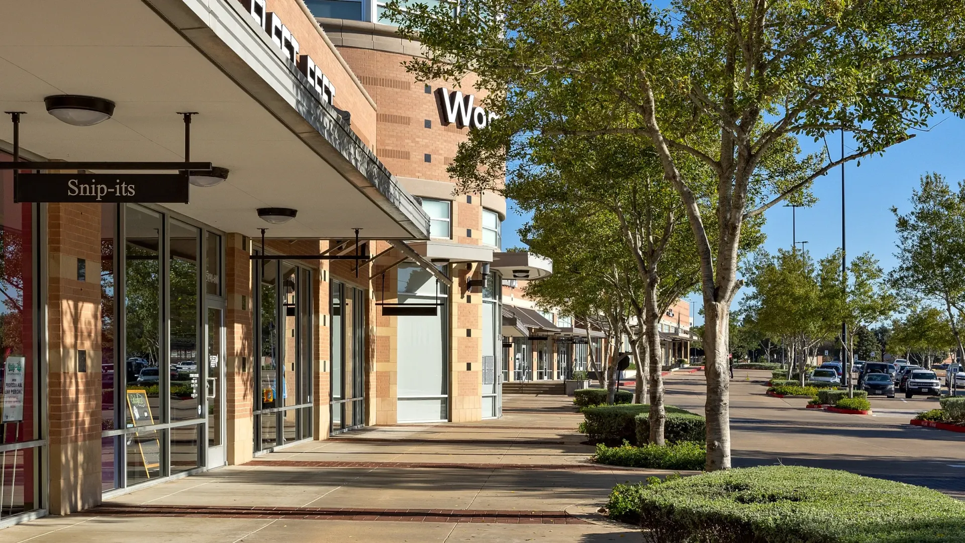A row of stores are lined up on a sidewalk in a shopping center.