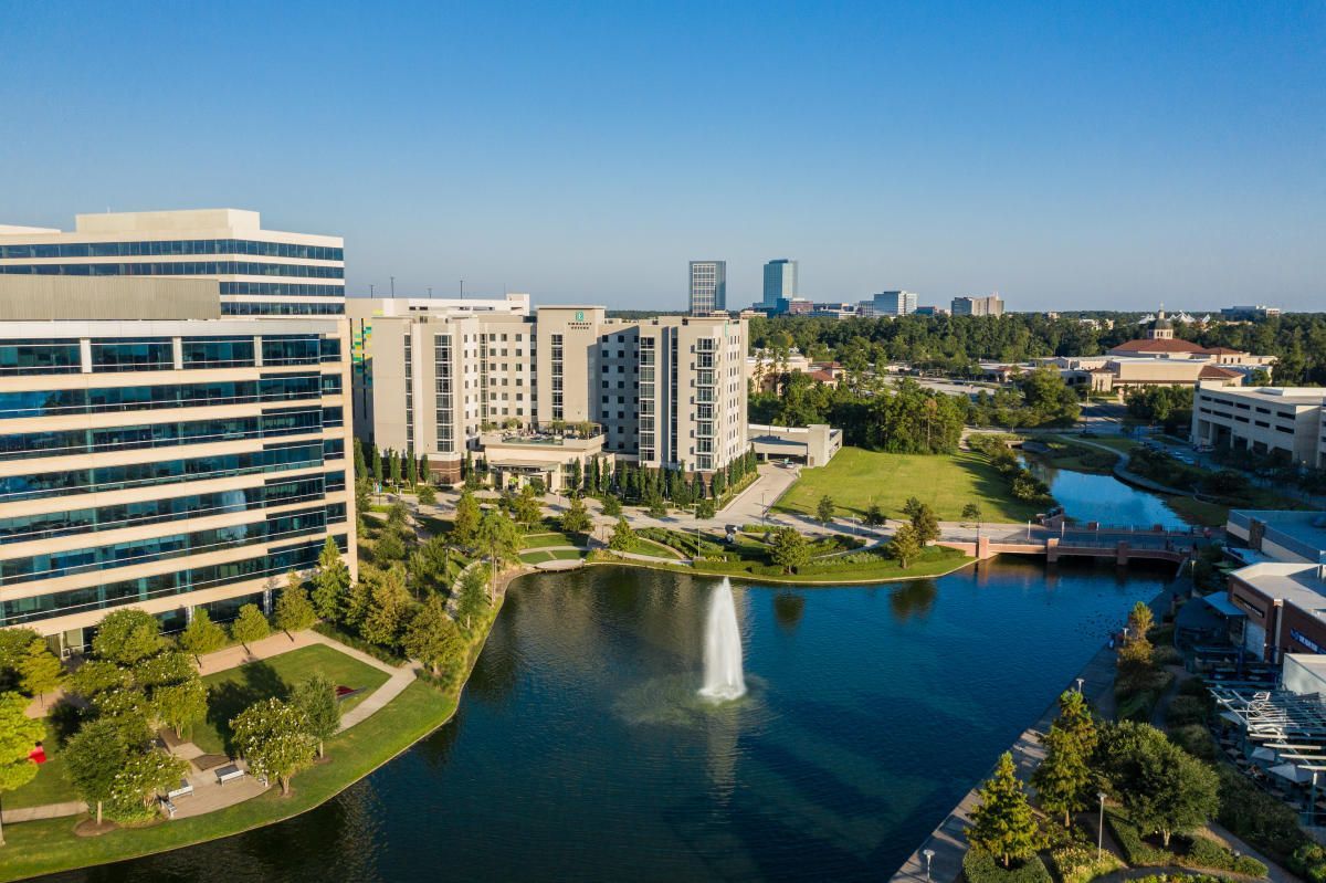 An aerial view of a city with a fountain in the middle of a lake surrounded by buildings.