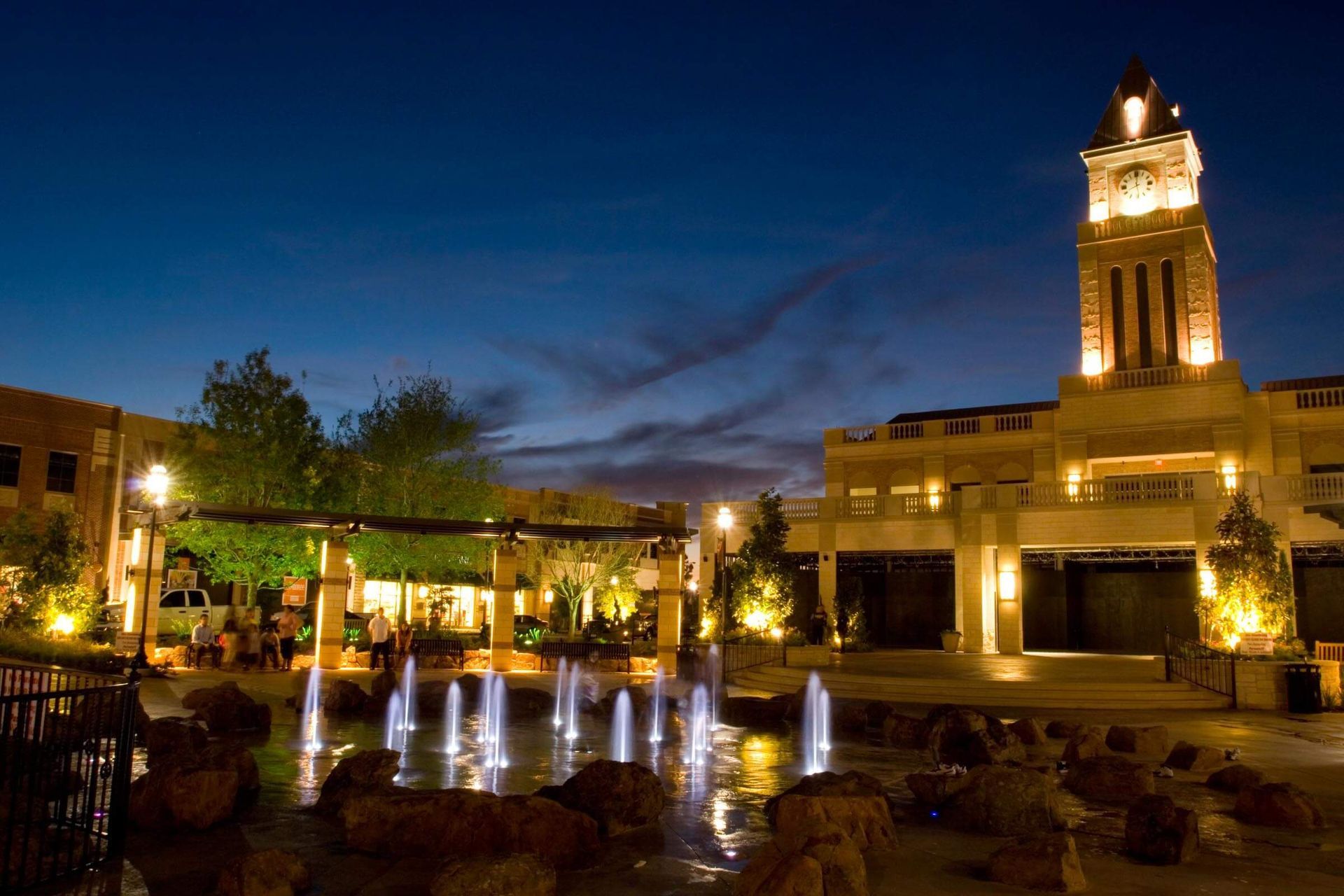A fountain in front of a clock tower at night