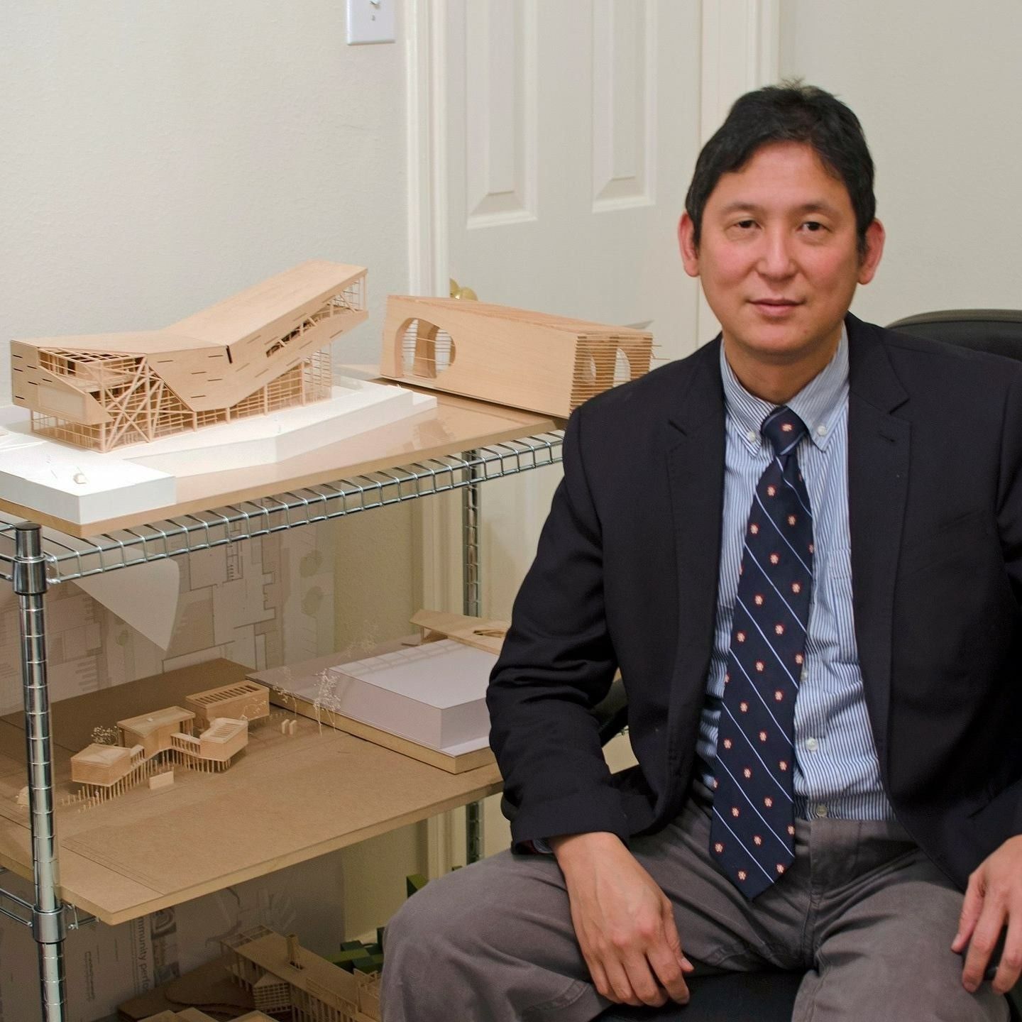 A man in a suit and tie is sitting in front of a shelf with models on it