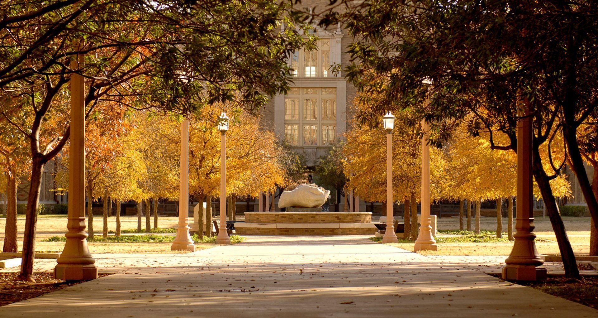 A walkway with trees and a fountain in the background