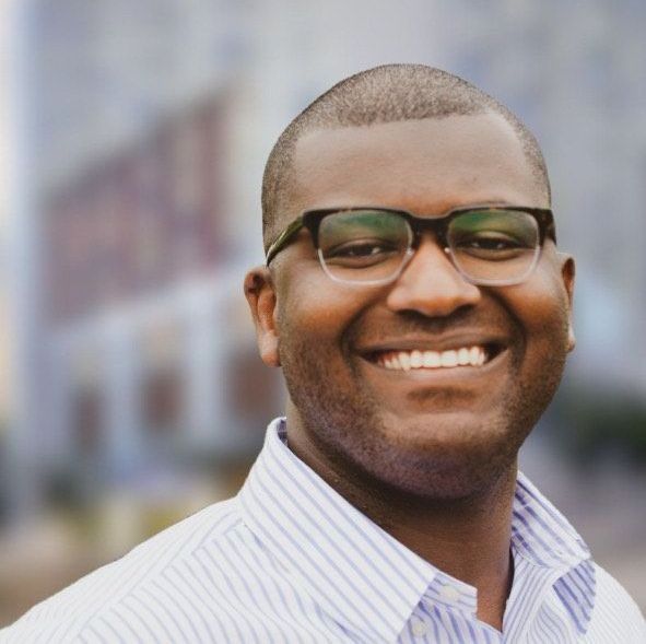 A man wearing glasses and a striped shirt smiles for the camera