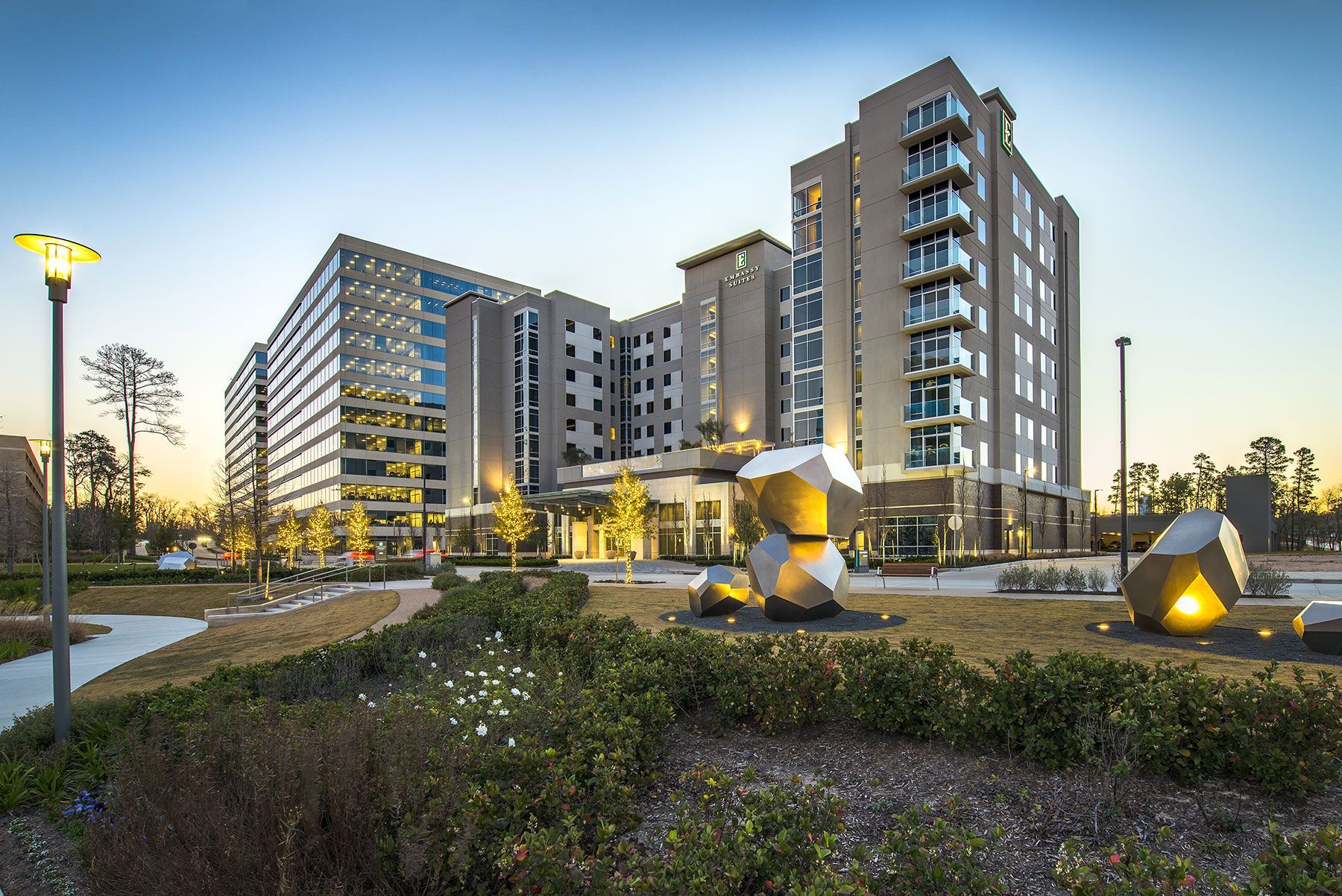 A large building with a lot of windows is surrounded by trees and bushes.
