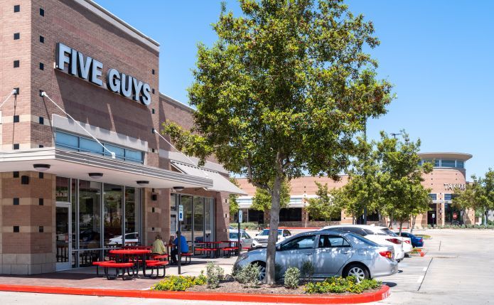 A five guys restaurant with cars parked in front of it.