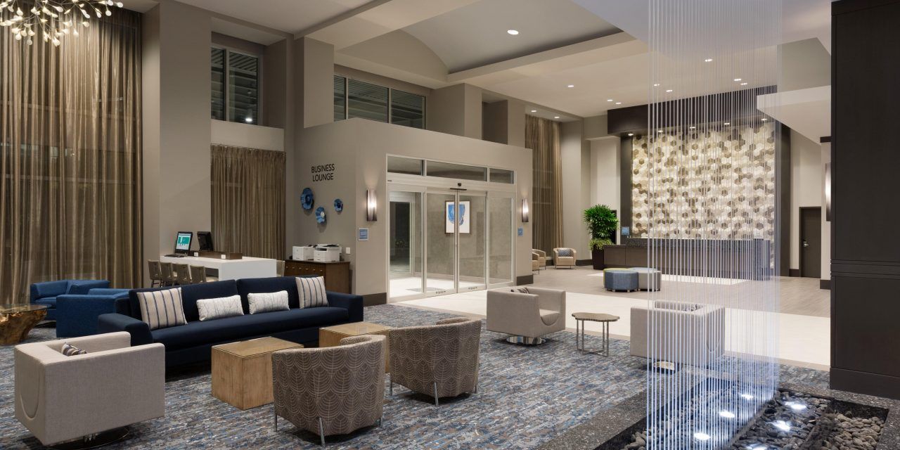 A hotel lobby with a couch , chairs , tables and a fountain.