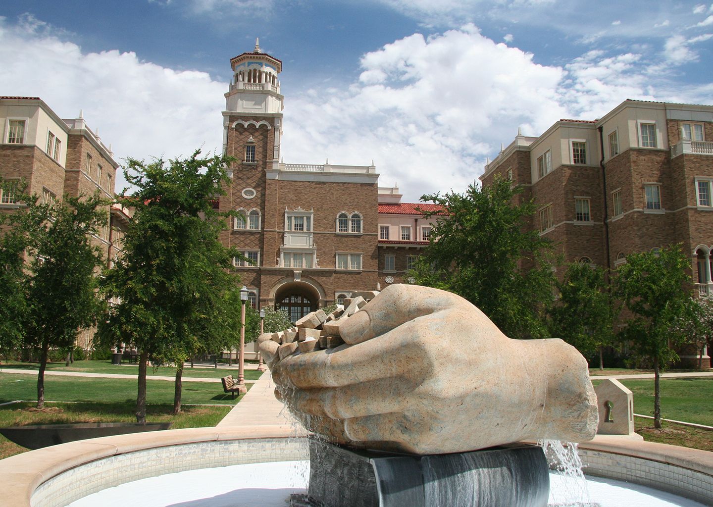 A fountain with a statue of a hand in front of a brick building