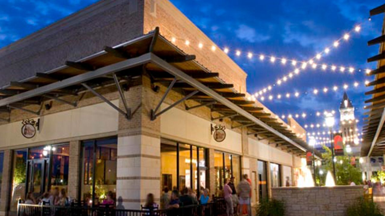 A group of people are sitting outside of a restaurant at night.