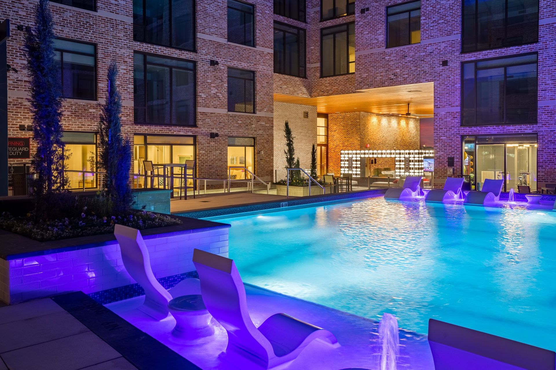 A large swimming pool is lit up at night in front of a building.
