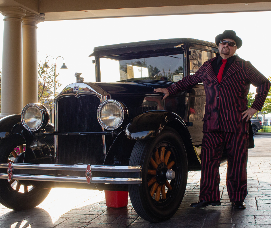 A man in a suit is standing next to an old car