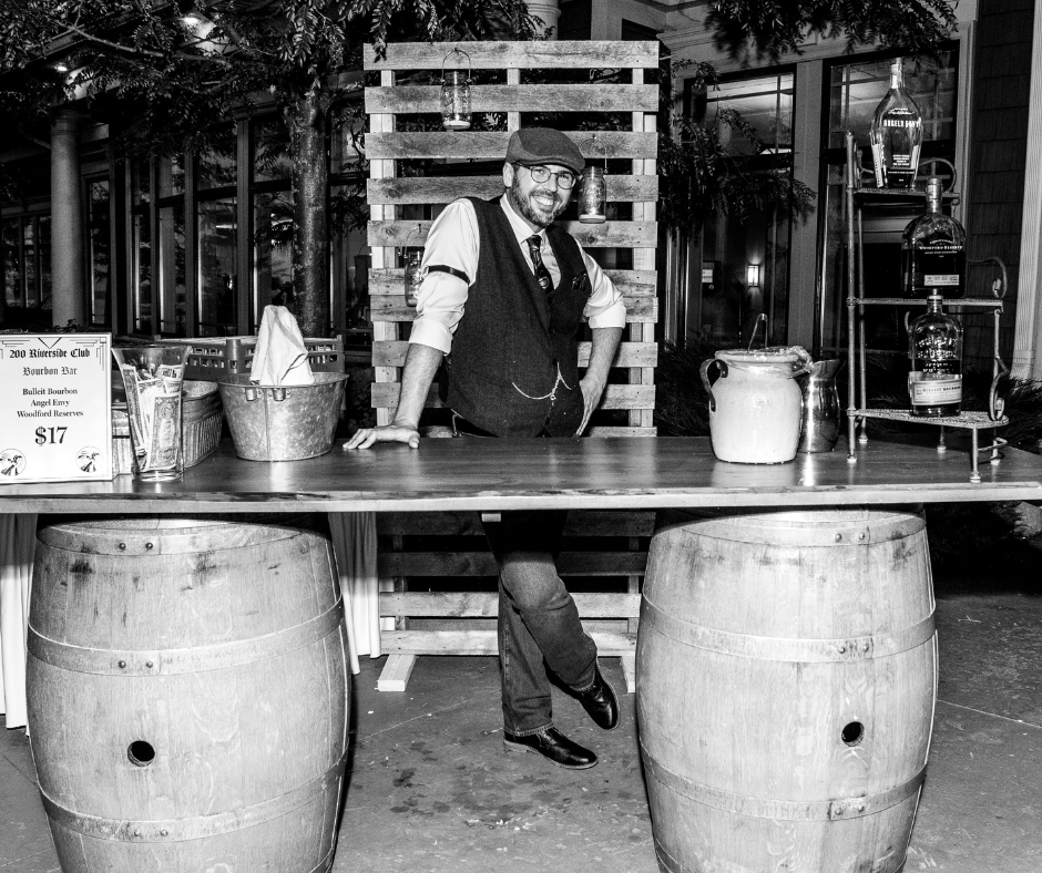 A man is standing at a table with two wooden barrels.