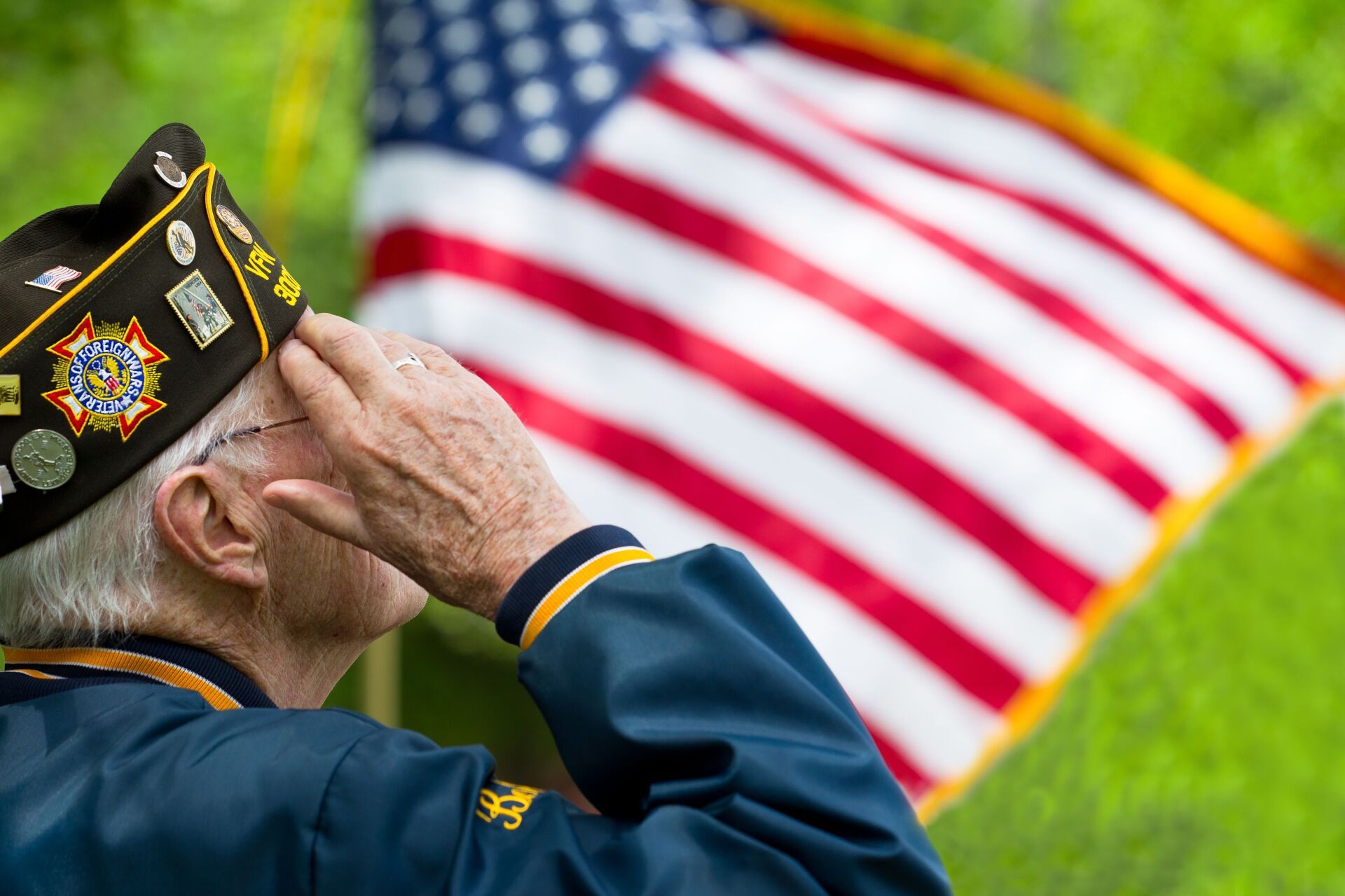 A man in a military uniform salutes in front of an american flag.