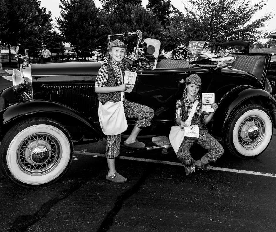 A black and white photo of two people standing next to an old car