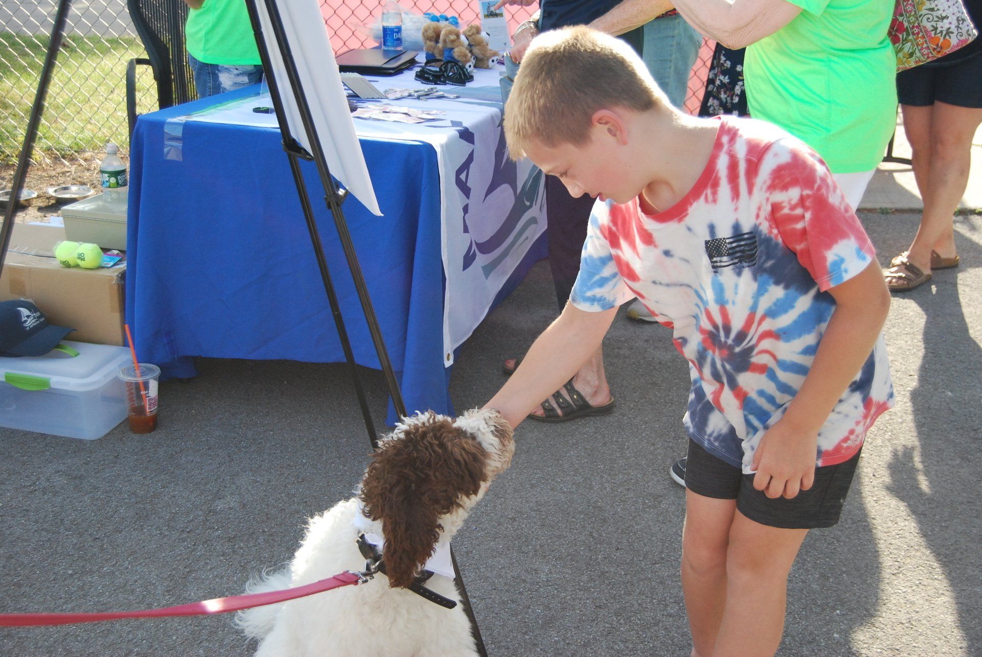 A boy in a tie dye shirt petting a dog