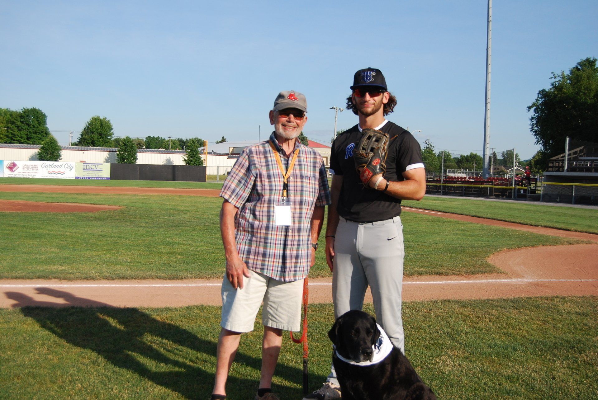 Two men and a dog are posing for a picture on a baseball field.