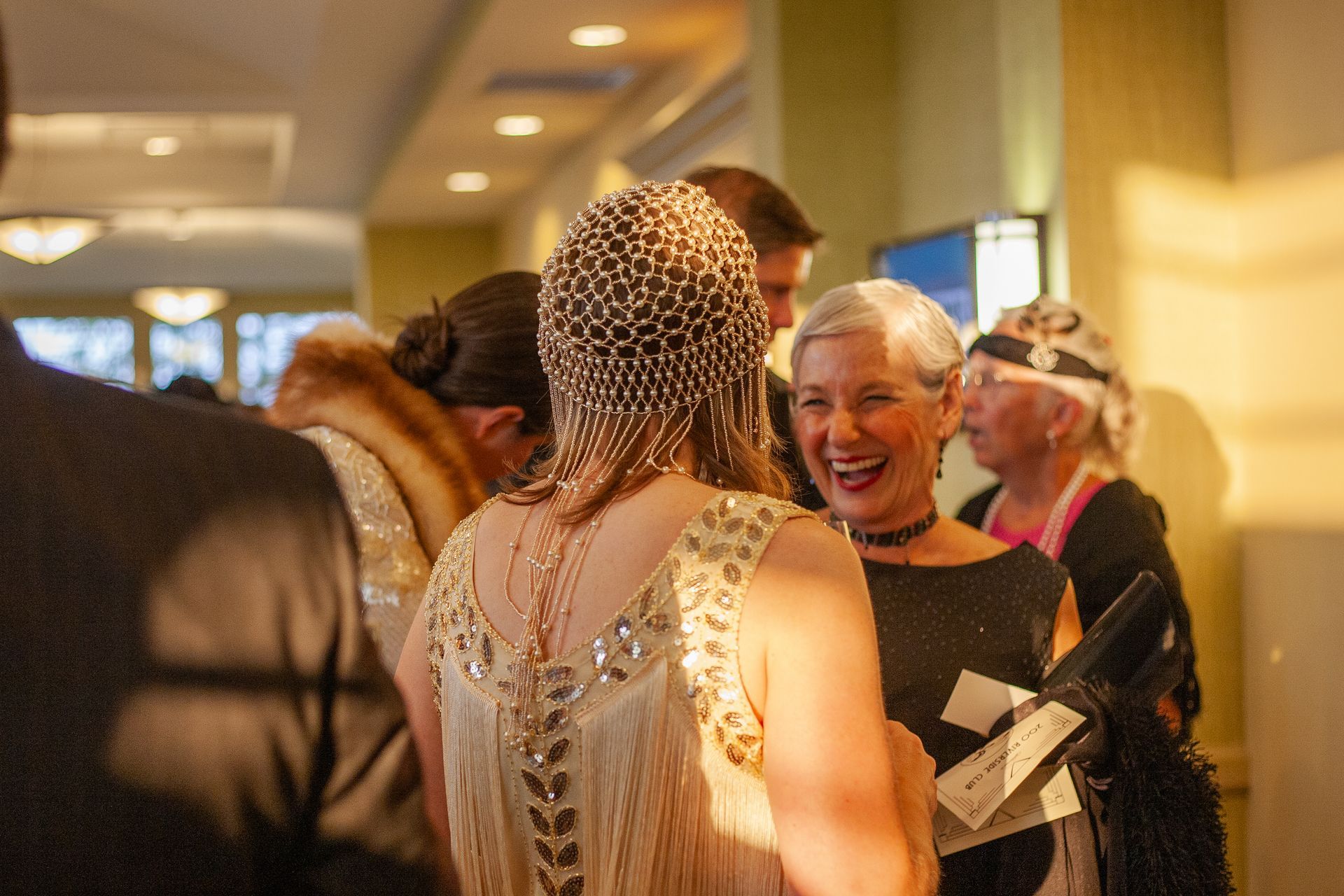 A woman in a dress is talking to a group of people in a room.