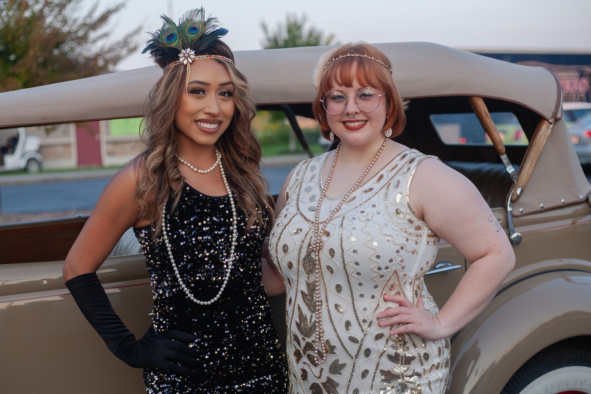 Two women are posing for a picture in front of an old car.