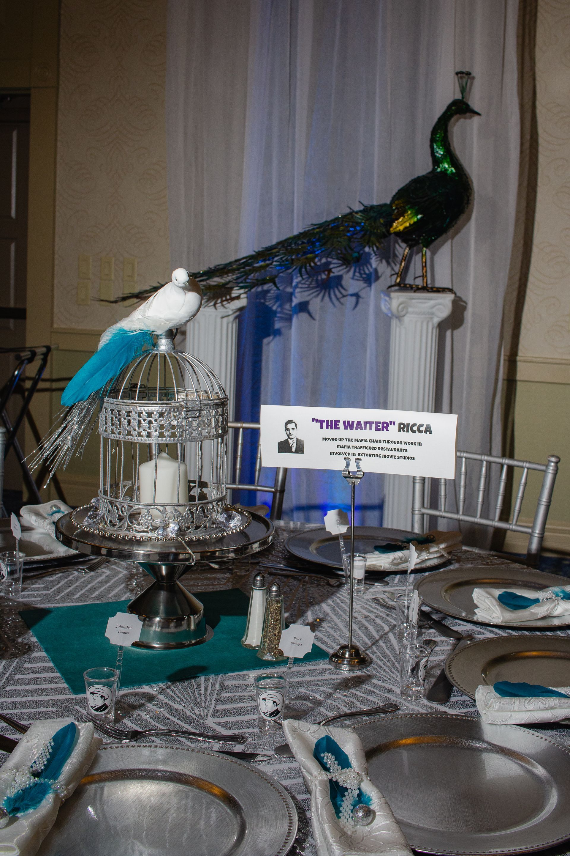 A peacock is sitting on top of a table with plates and glasses.