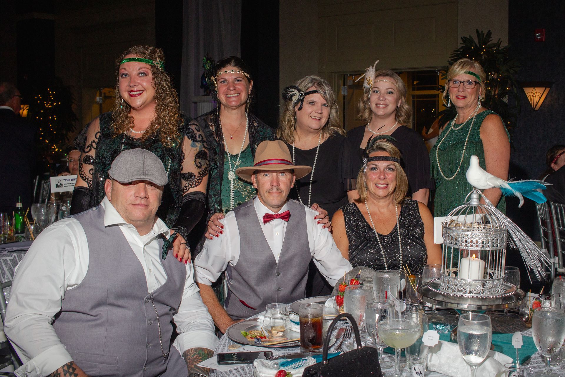 A group of people dressed in flapper costumes are posing for a picture at a table.