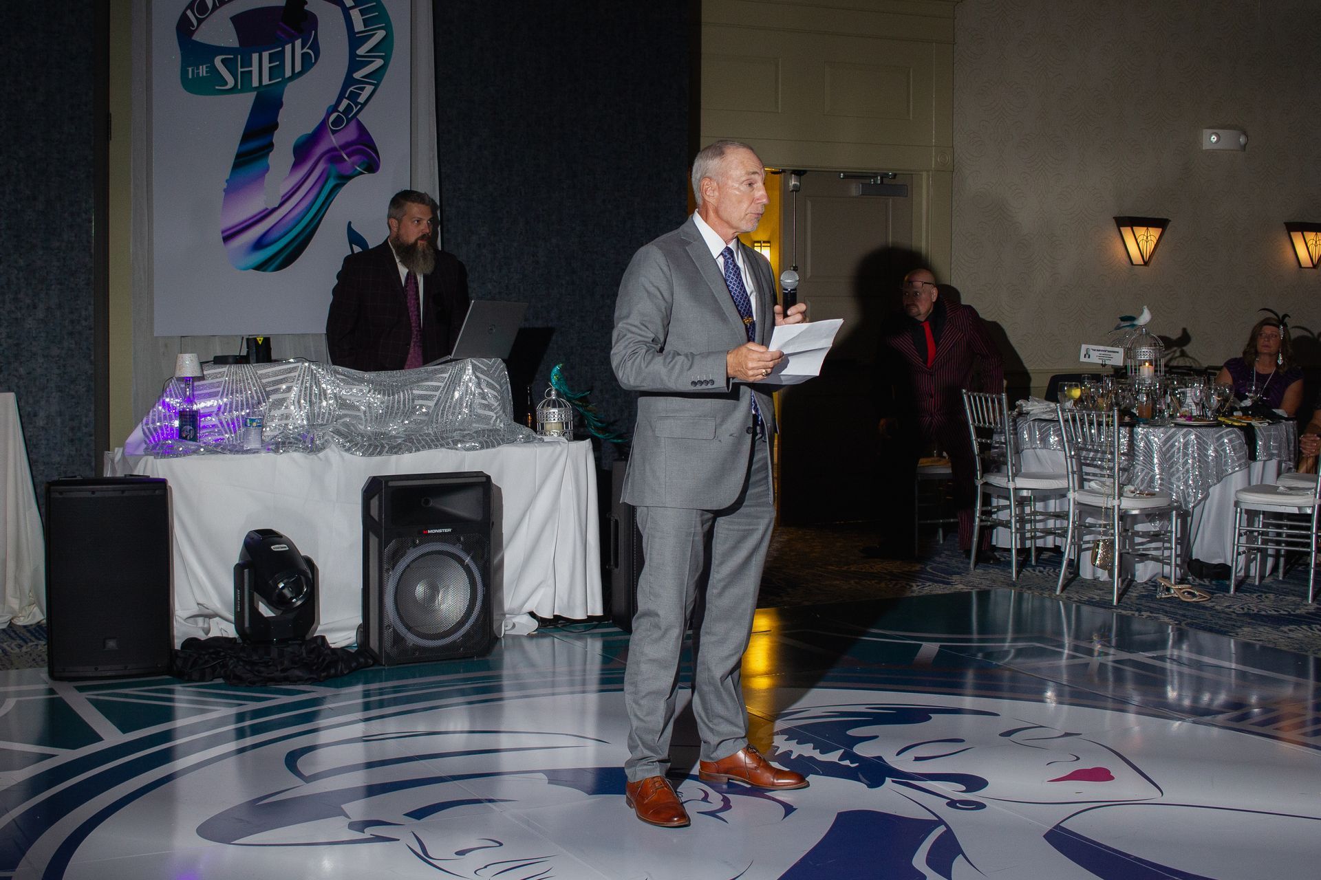 A man in a suit is standing on a dance floor giving a speech.