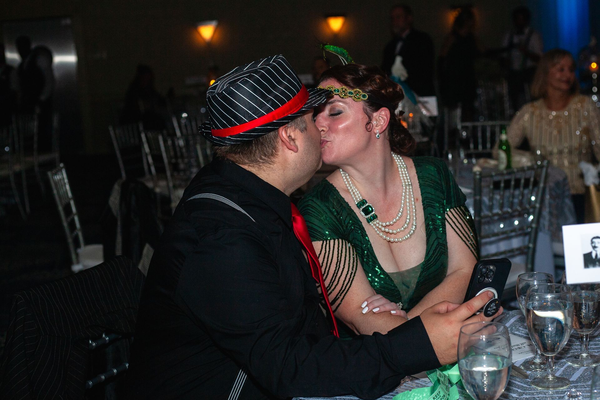 A man and woman are kissing at a table at a party.