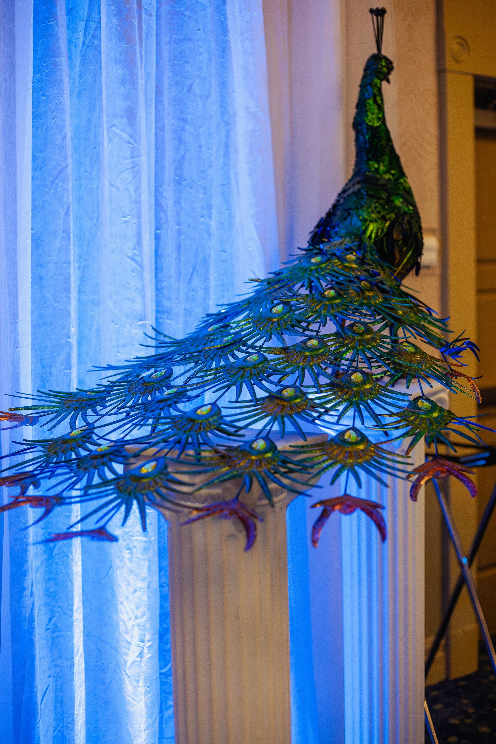 A peacock statue is hanging from the ceiling in front of a window.