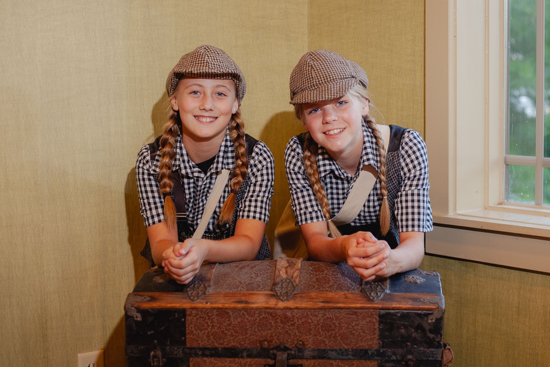 Two young girls are sitting on a trunk in a room.