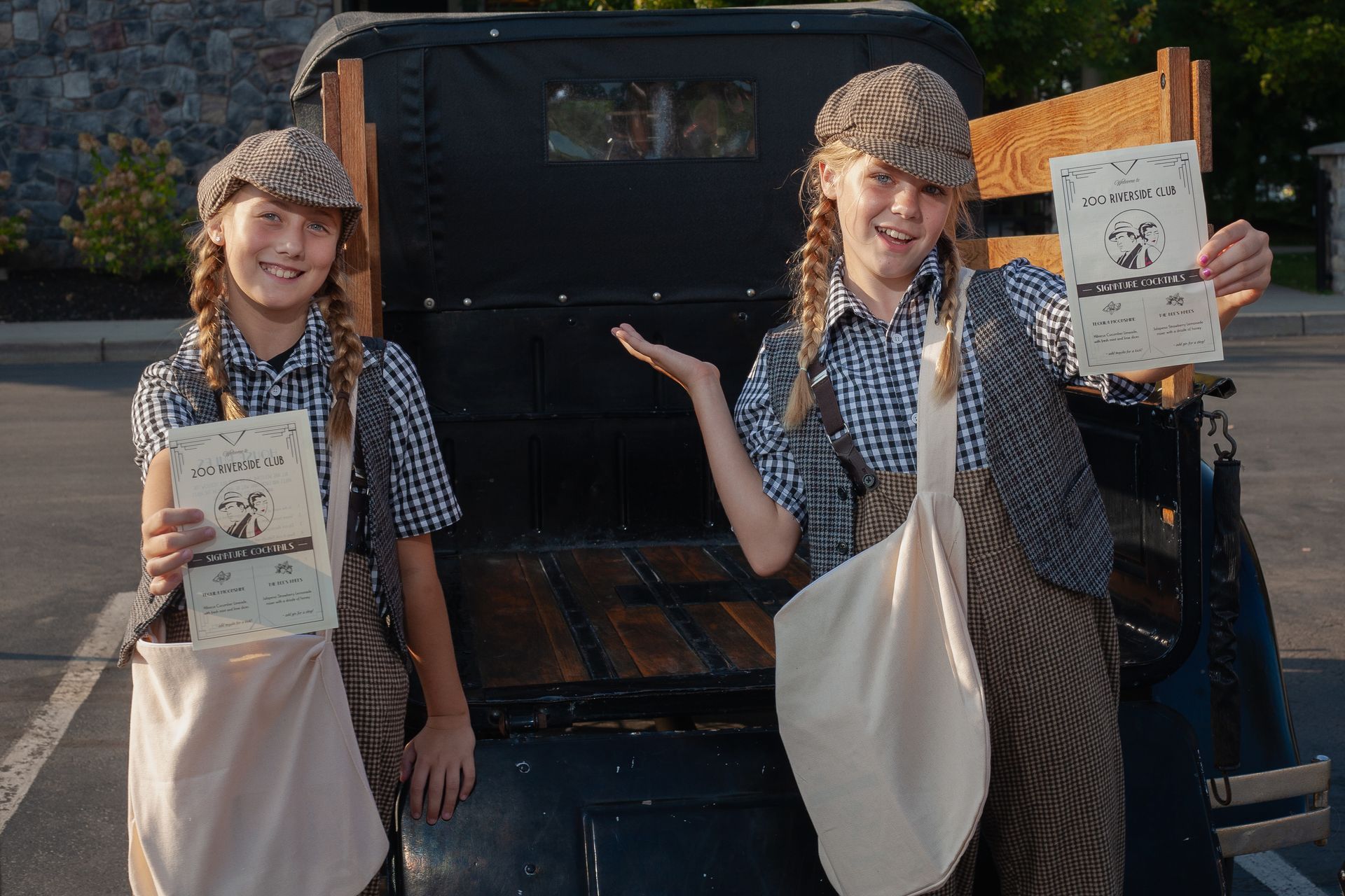 Two young girls are standing in front of a truck holding papers