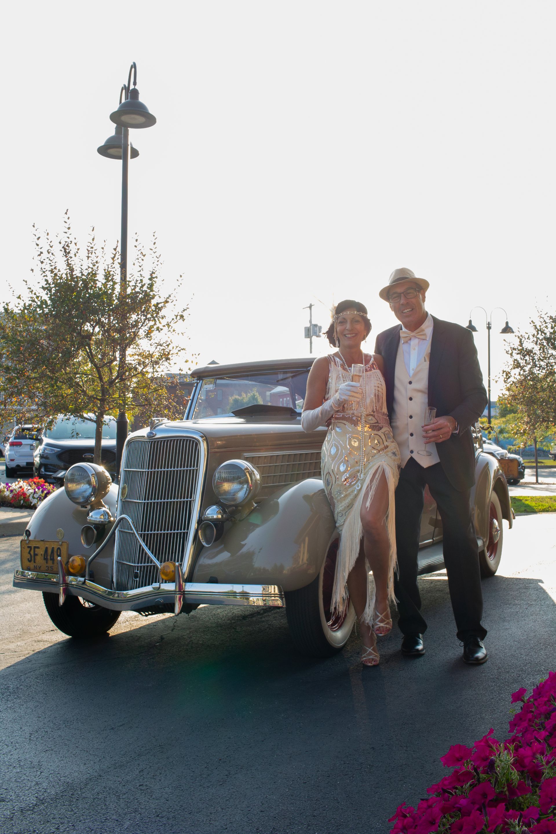 A bride and groom are posing for a picture in front of a vintage car.