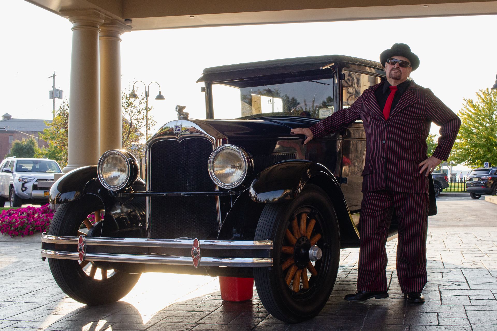 A man in a suit and tie is standing next to an old car
