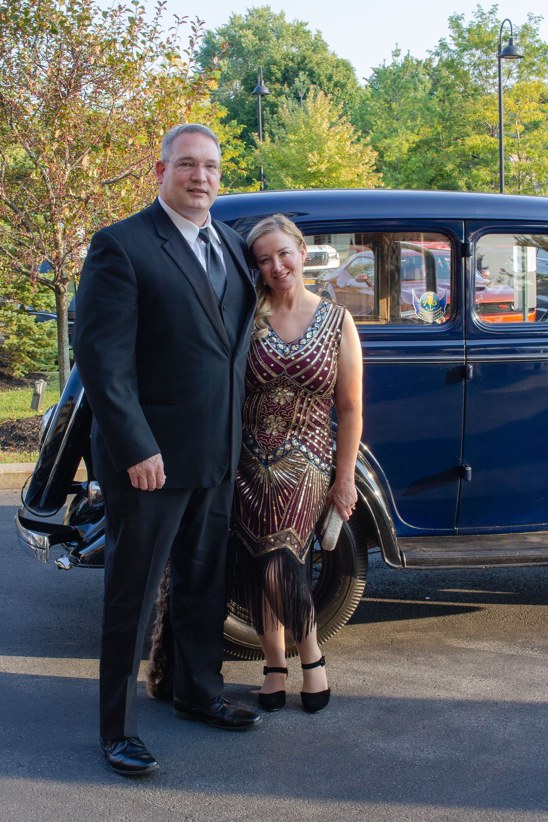 A man and a woman are posing for a picture in front of an old car.