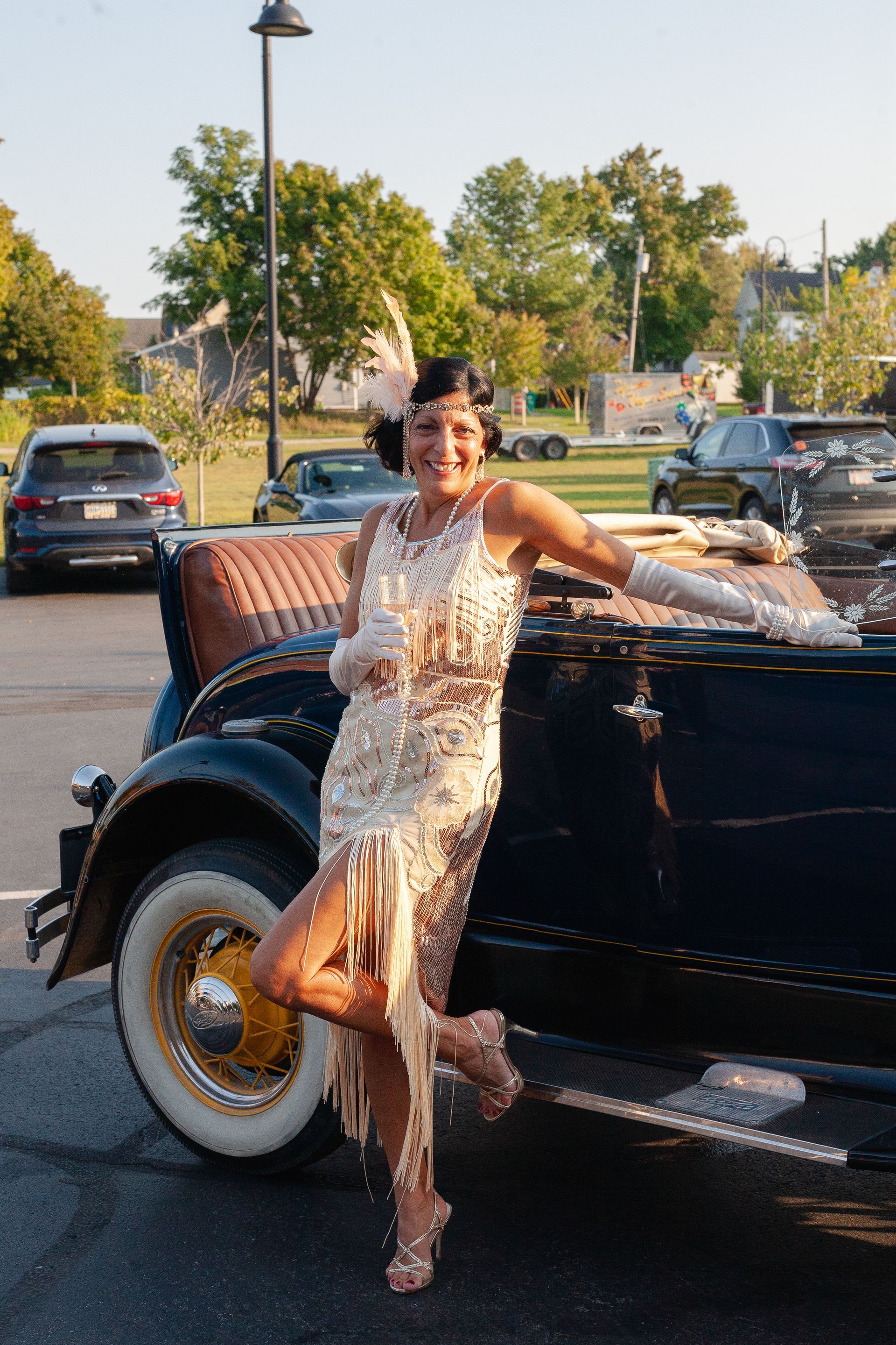 A woman in a flapper dress is standing next to an old car.