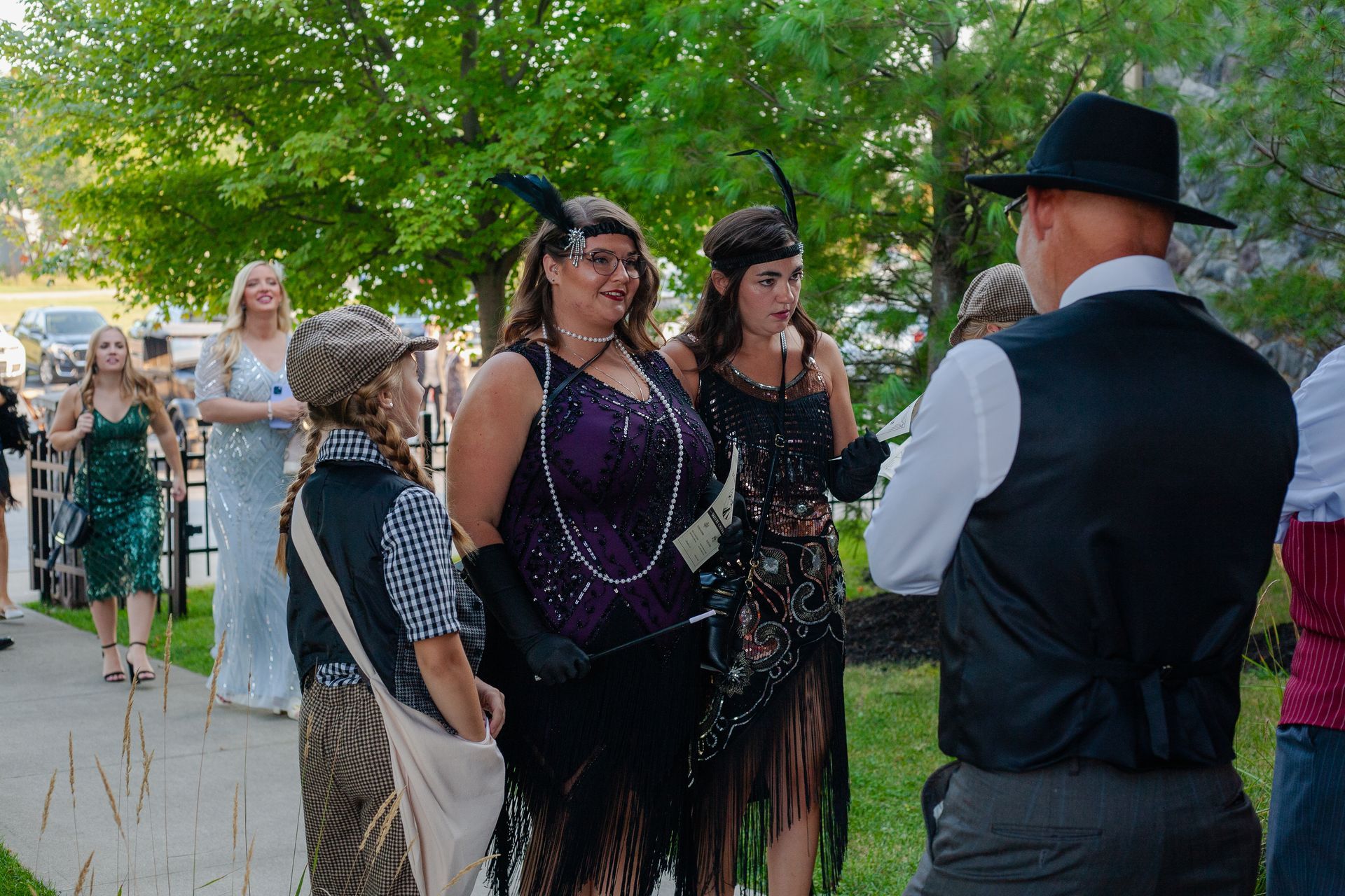 A group of people dressed in flapper costumes are standing on a sidewalk.