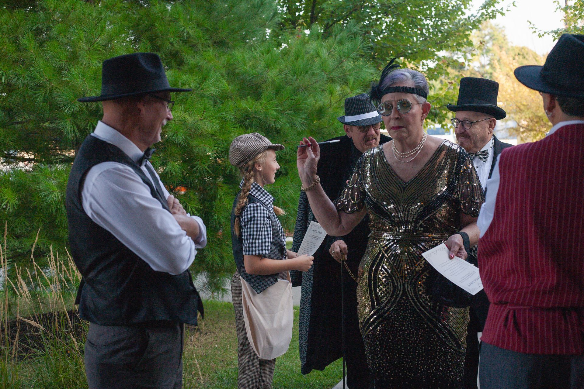 A group of people in costume are standing in a park talking to each other.