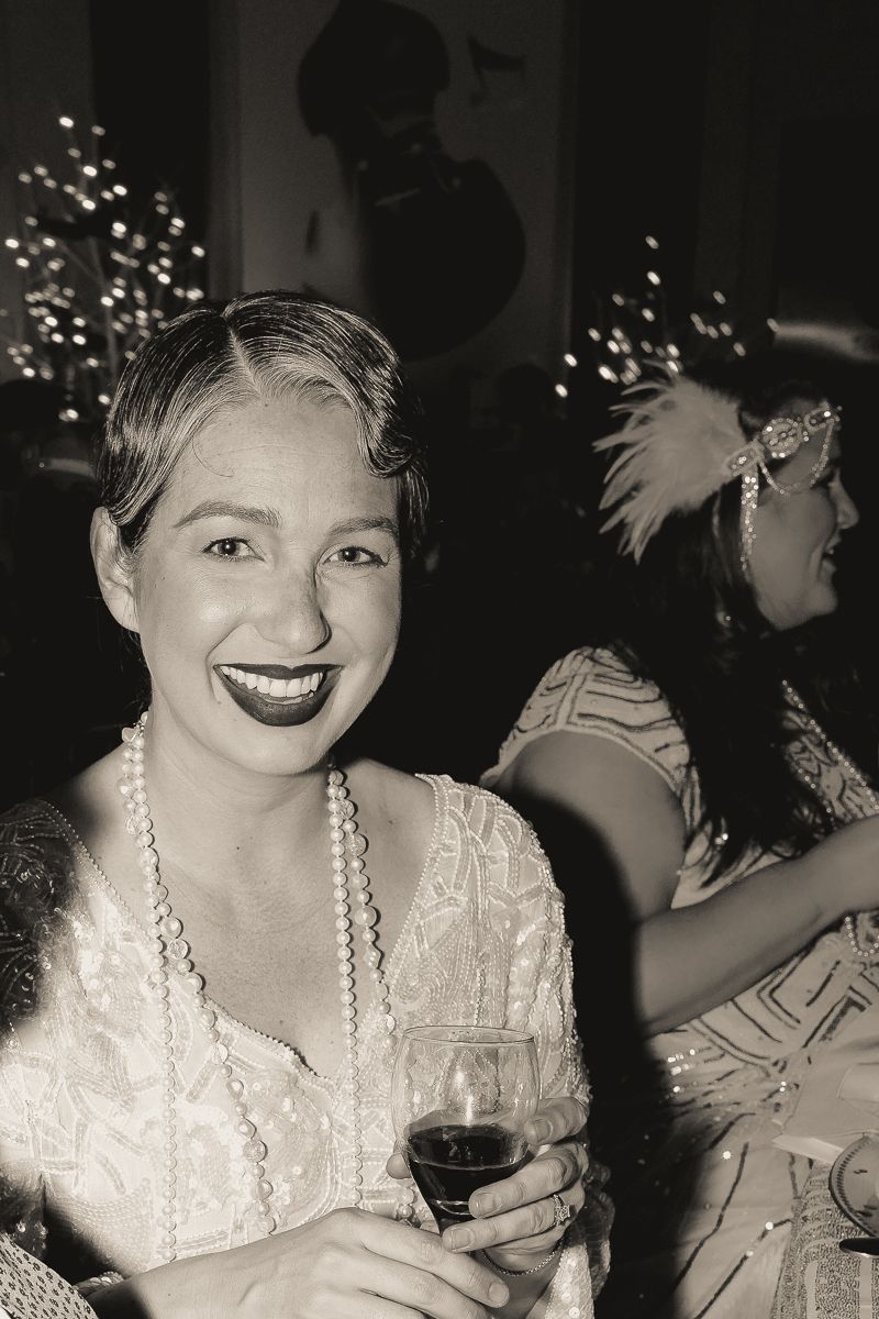 A woman is holding a glass of wine and smiling in a black and white photo.
